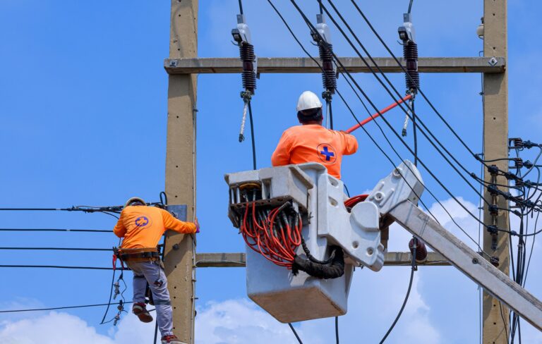 Electricians with disconnect stick and boom lift are installing electrical system on power pole