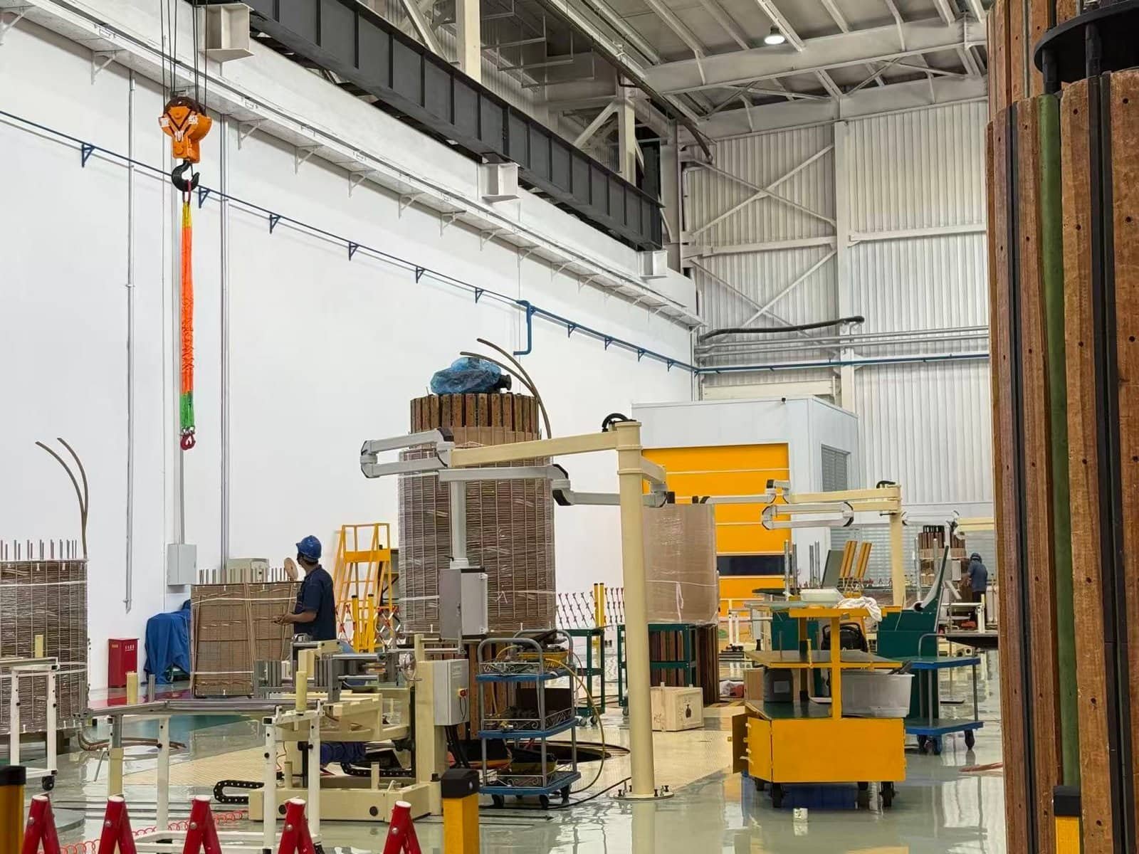High-voltage transformer manufacturing inside an industrial facility, featuring specialized machinery, worker in safety gear, and transformer components under assembly, demonstrating advanced transformer production technology.