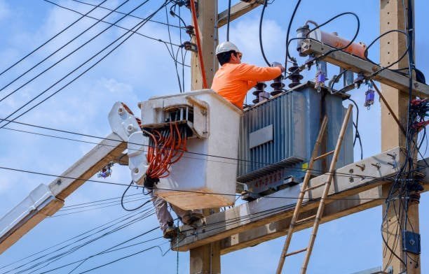 High-voltage power transformer maintenance on utility pole with technician working in a sunny outdoor setting.