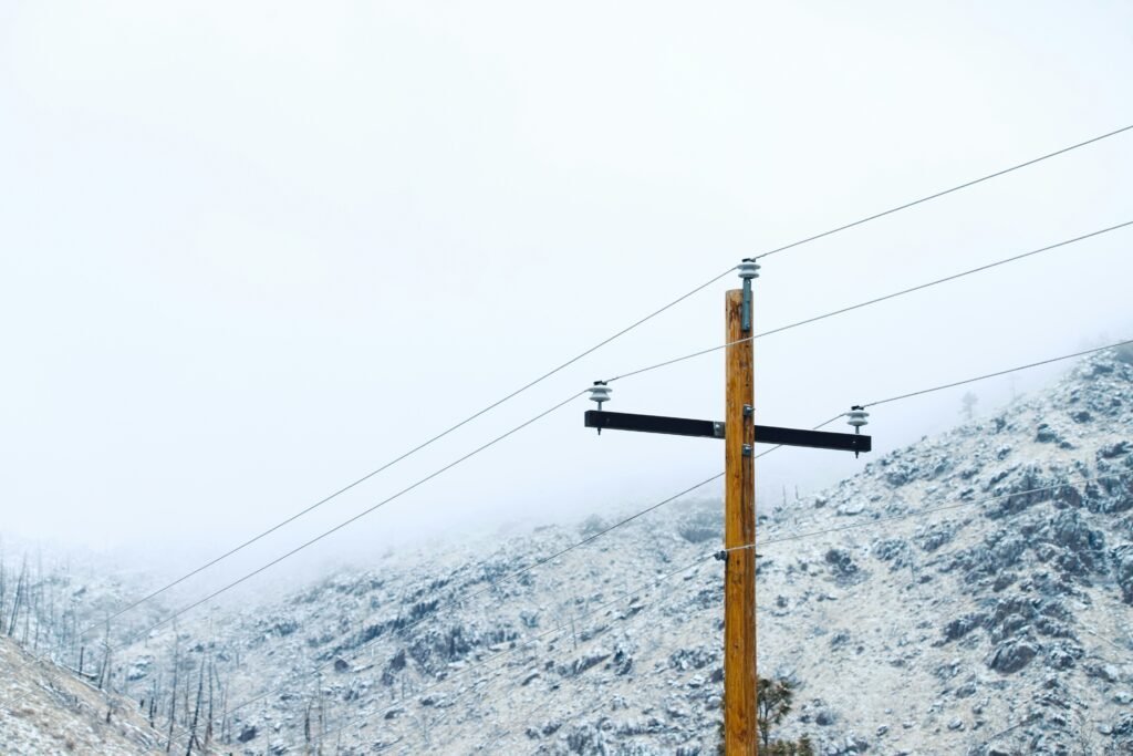 High-voltage power line pole in a snowy mountain landscape, emphasizing electrical infrastructure and winter scenery.