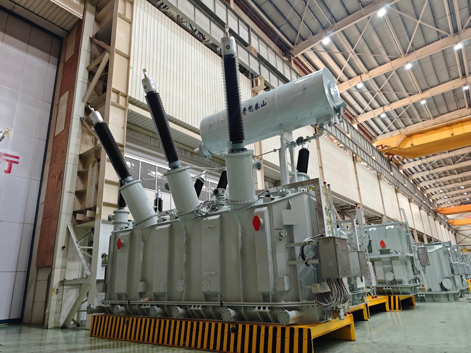 High-voltage power transformer at Taishan Transformer factory, showcasing advanced electrical equipment and manufacturing expertise in a spacious industrial setting.