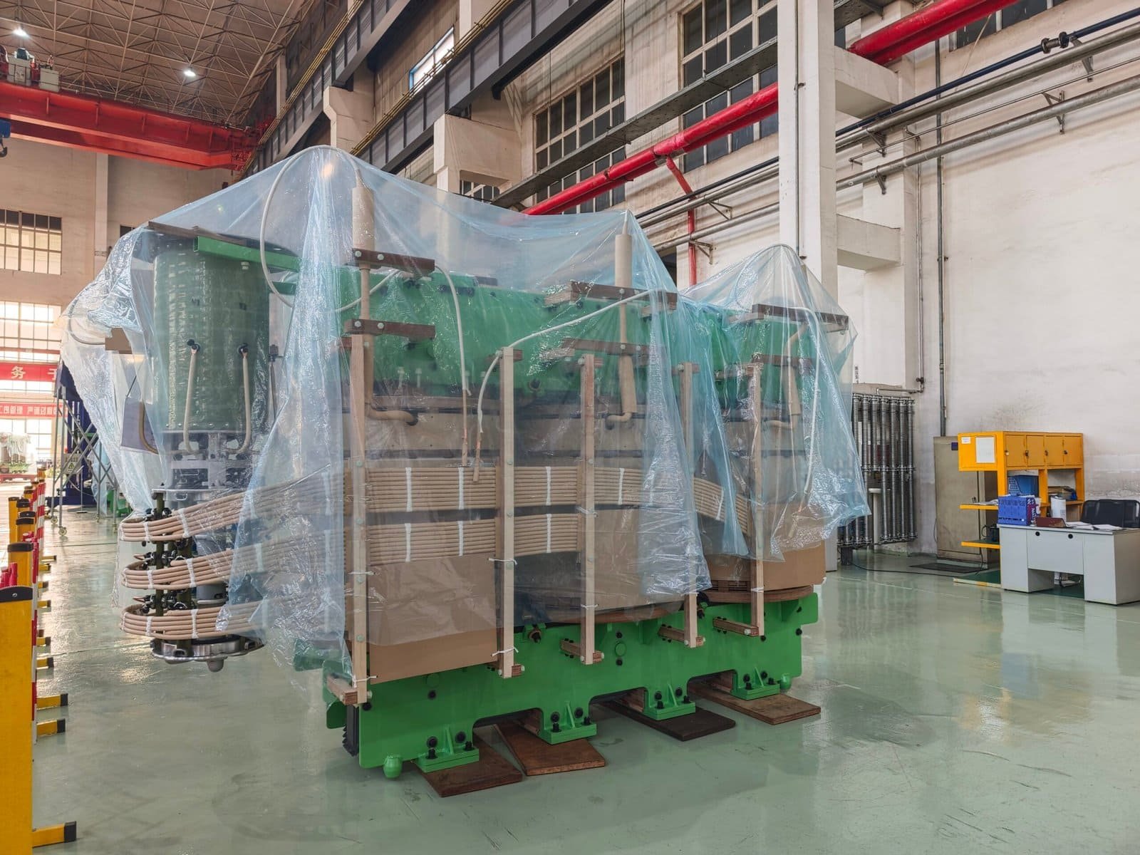 High-voltage power transformer at Taishan Transformer factory, covered with protective plastic film, ready for installation or transportation in an industrial setting.