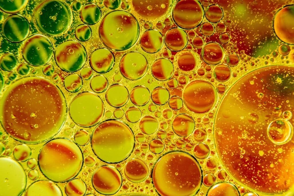A colorful abstract image of various-sized oil droplets suspended in water, showcasing vibrant green, yellow, and orange hues with a dynamic, bubbly texture.