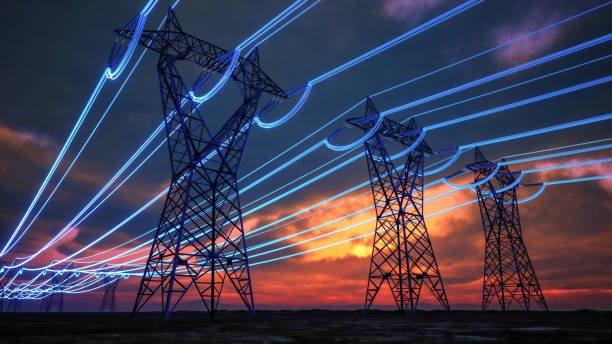 High-voltage power lines and transmission towers at sunset with light trails from electrical currents.