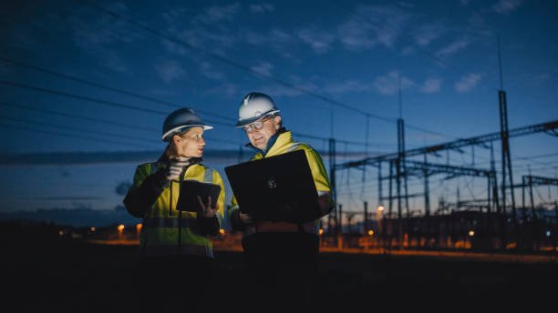 Two engineers in safety gear inspecting electrical infrastructure at dusk, highlighting power transformer maintenance and engineering expertise.